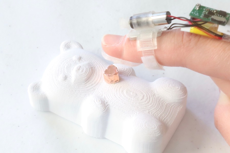 A user wearing the fingerpad device touches a 3D-printed teddy bear made from rigid material.