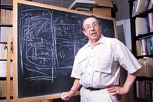 Bernard Silberman stands with one hand on hip in front of a chalkboard.