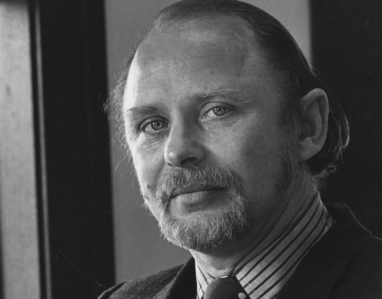 Edward Wasiolek, in suit and tie, stands by a door.