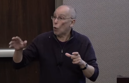 William Meadow, wearing glasses, gestures while lecturing.