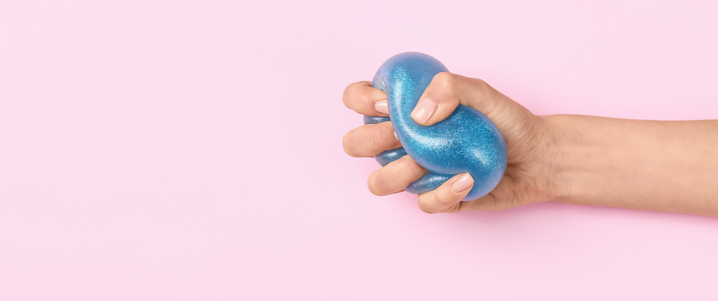 a hand squeezing a glittery blue stress ball on pink background
