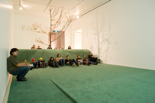 Visitors watch Guy Ben-Ner's Wild Boy (2004) from a carpeted hill that re-creates the woodland set the artist built in his kitchen. Photo by Jim Newberry.