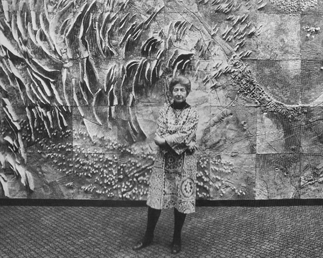 Black-and-white photo of a woman standing in front of a large ceramic mural