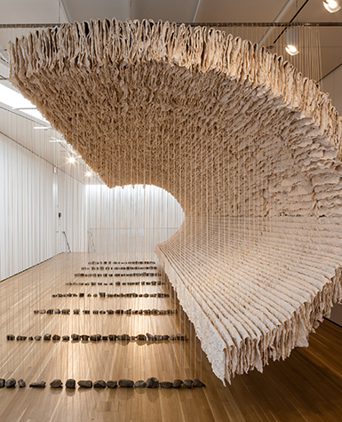 A wave-like sculpture made from thousands of sheets of crumpled paper, bamboo rods, strings, and rocks.