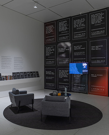 Gallery installation showing a TV monitor on a wall covered with posters and a pair of chairs