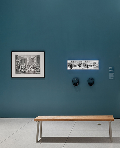 A large print hangs side-by-side with two video monitors in a museum exhibition