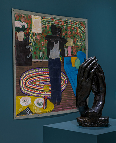 A bronze sculpture of two hands touching rests on a plinth in front of a painting of a dancing couple