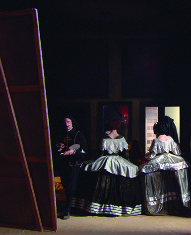 In a painting-liked photograph, two women and attendants pose while an artist paints a large canvas