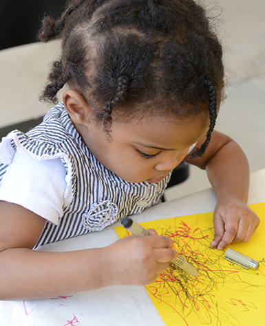 A child drawing with colored pens on yellow paper