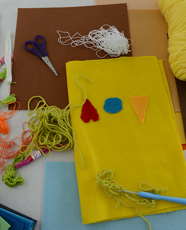A craft table with a yellow rectangle of felt with a red heart, blue circle, and yellow triangle on it