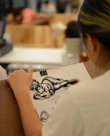 Seen from behind, a person sketches during a figure drawing session.