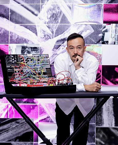 Portrait of Kikù Hibino leaning on a table with a synthesizer