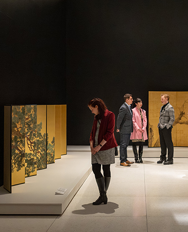 Museum guests look at painted folding screens on gold leaf