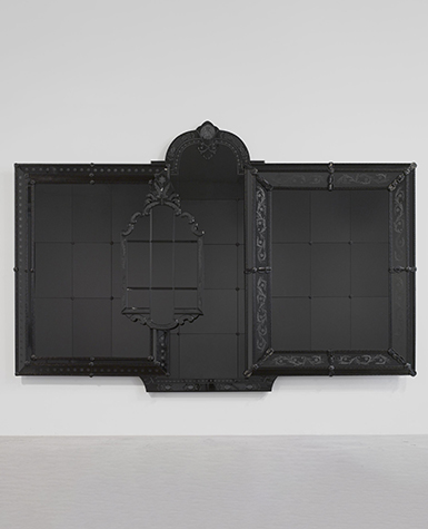 A ornate black mirror hangs on a gallery wall