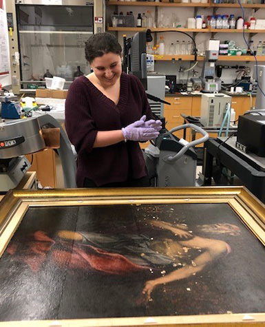 A student wearing protective gloves looks at a painting laid flat on a table