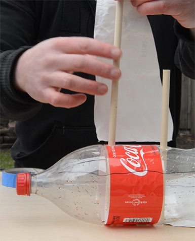 Close up of a person's hands adding a sail to a plastic Coke bottle