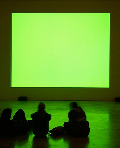 People sit on the floor in front of a green colored projection screen